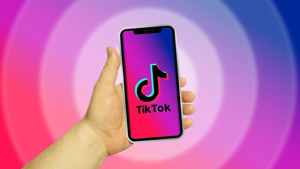 Main qui tient un téléphone avec TikTok en fond d'écran.